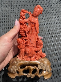A Chinese carved red coral 'Goddess and Boys' group on a wooden stand, 19/20th C.