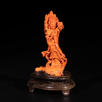 A Chinese red coral Guanyin holding a lotus on wooden stand, 19/20th C.