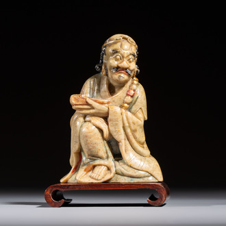 A Chinese gilt-polychromed soapstone Luohan on a wooden stand, 19th C.
