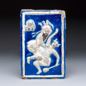 A Persian relief-moulded blue-ground tile depicting Fateh 'Ali Shah in the guise of Rustam slaying the White Div, Qajar, 19th C.