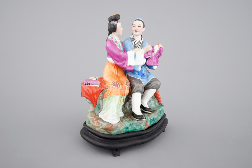 A Chinese porcelain model of an amorous couple, on wooden stand, 20th C.