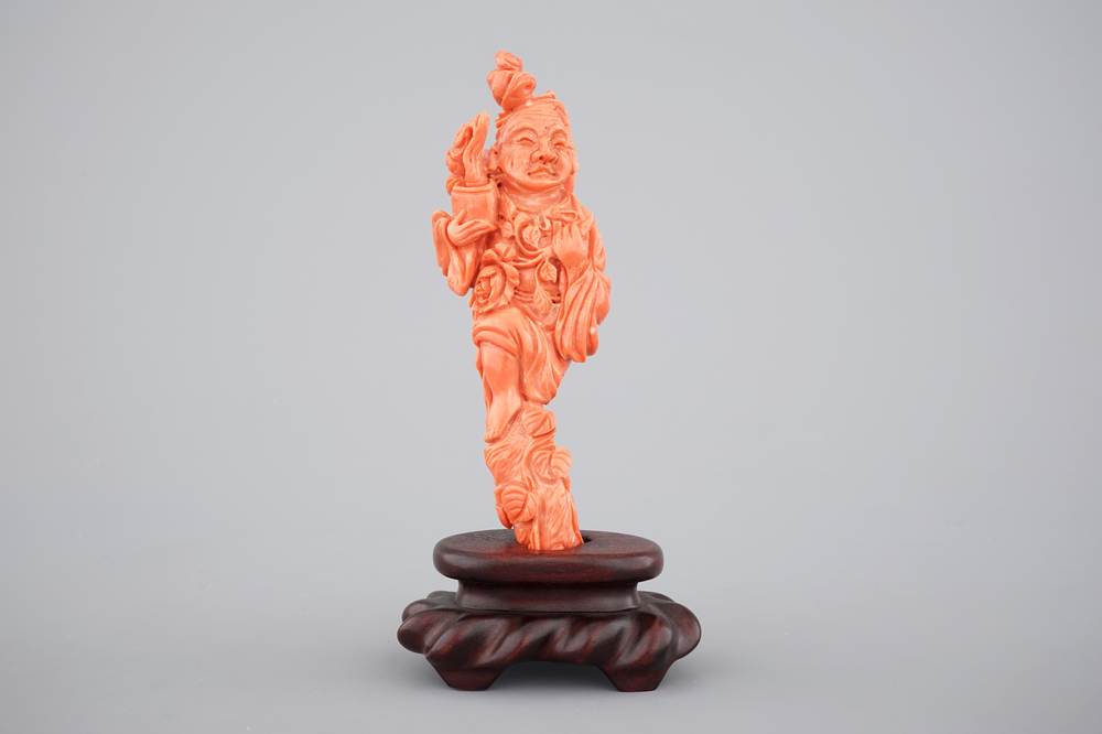 A Chinese carved red coral figure on a wooden stand, 19/20th C.
