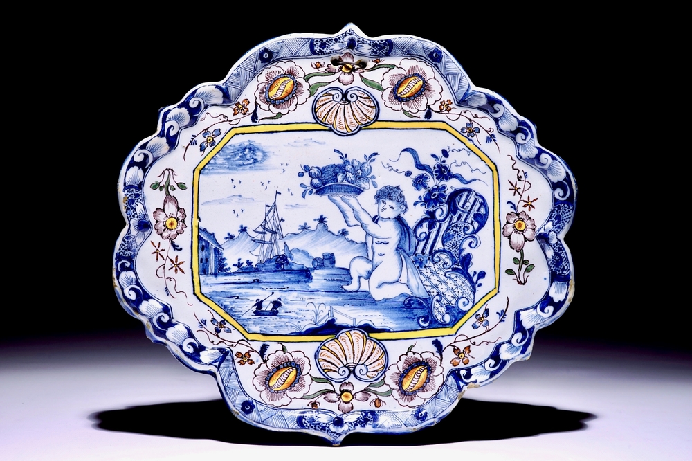 Une plaque en fa&iuml;ence de Delft polychrome &agrave; d&eacute;cor d'un putto portant un panier de fruits, 18&egrave;me
