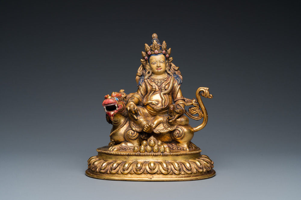 A Tibetan gilt bronze group of Jambhala on his lion, 19/20th C.