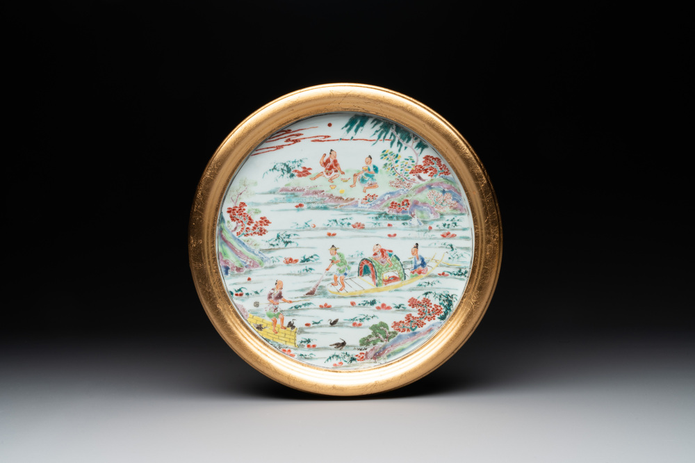 A Chinese famille rose plate with figures in a river landscape in gilt wooden frame, Yongzheng