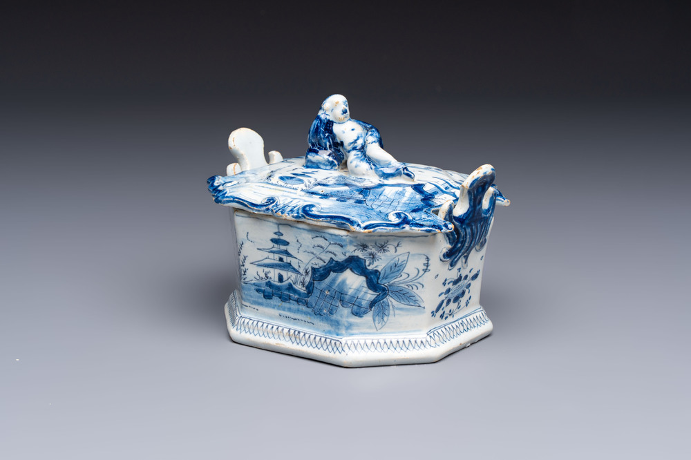 A blue and white Dutch Delft chinoiserie butter tub with a reclining figure finial, 18th C.