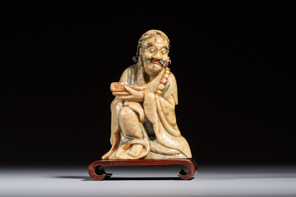 A Chinese gilt-polychromed soapstone Luohan on a wooden stand, 19th C.