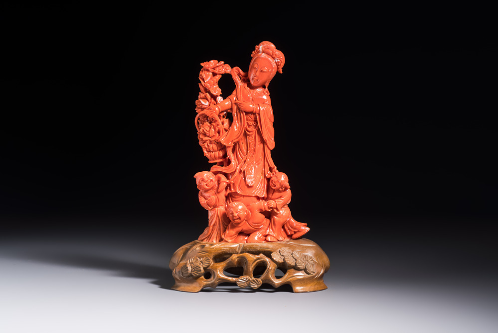 A Chinese carved red coral 'Goddess and Boys' group on a wooden stand, 19/20th C.