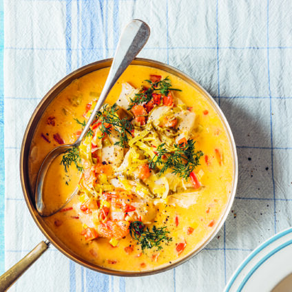 En traktörpanna med en gyllengul fiskgryta som står på en ljusblå bordsduk. Fiskgrytan är dekorerad med rom och dill.